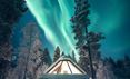 The northern lights over a glass roofed cabin at Aurora Village in Finnish Lapland
