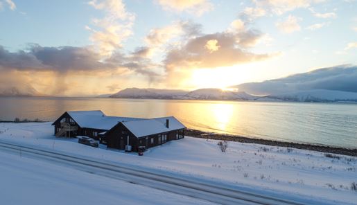 View of the Lyngen Experience Lodge over the water at sundown, Norway