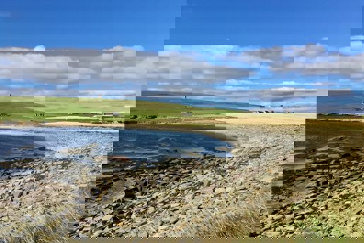 Stony beach and the blue sea on a sunny day in Orkney, Scotland.