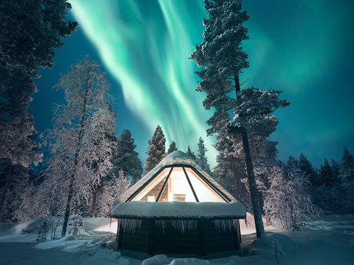 An aurora cabin under in a snowy forest under the Northern Lights sky in Lapland in winter