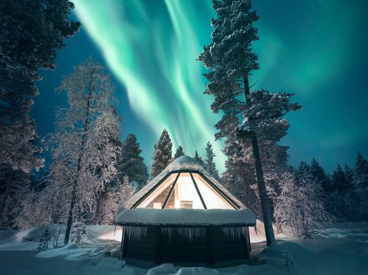 An aurora cabin under in a snowy forest under the Northern Lights sky in Lapland in winter